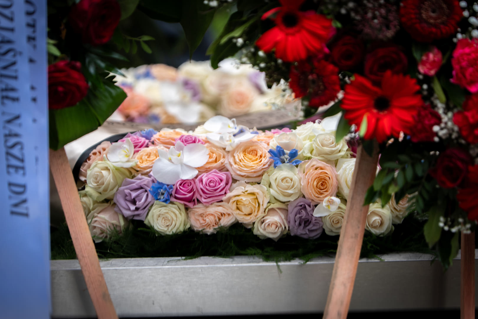 A spray of roses and a wreath of red gerberas at a grave