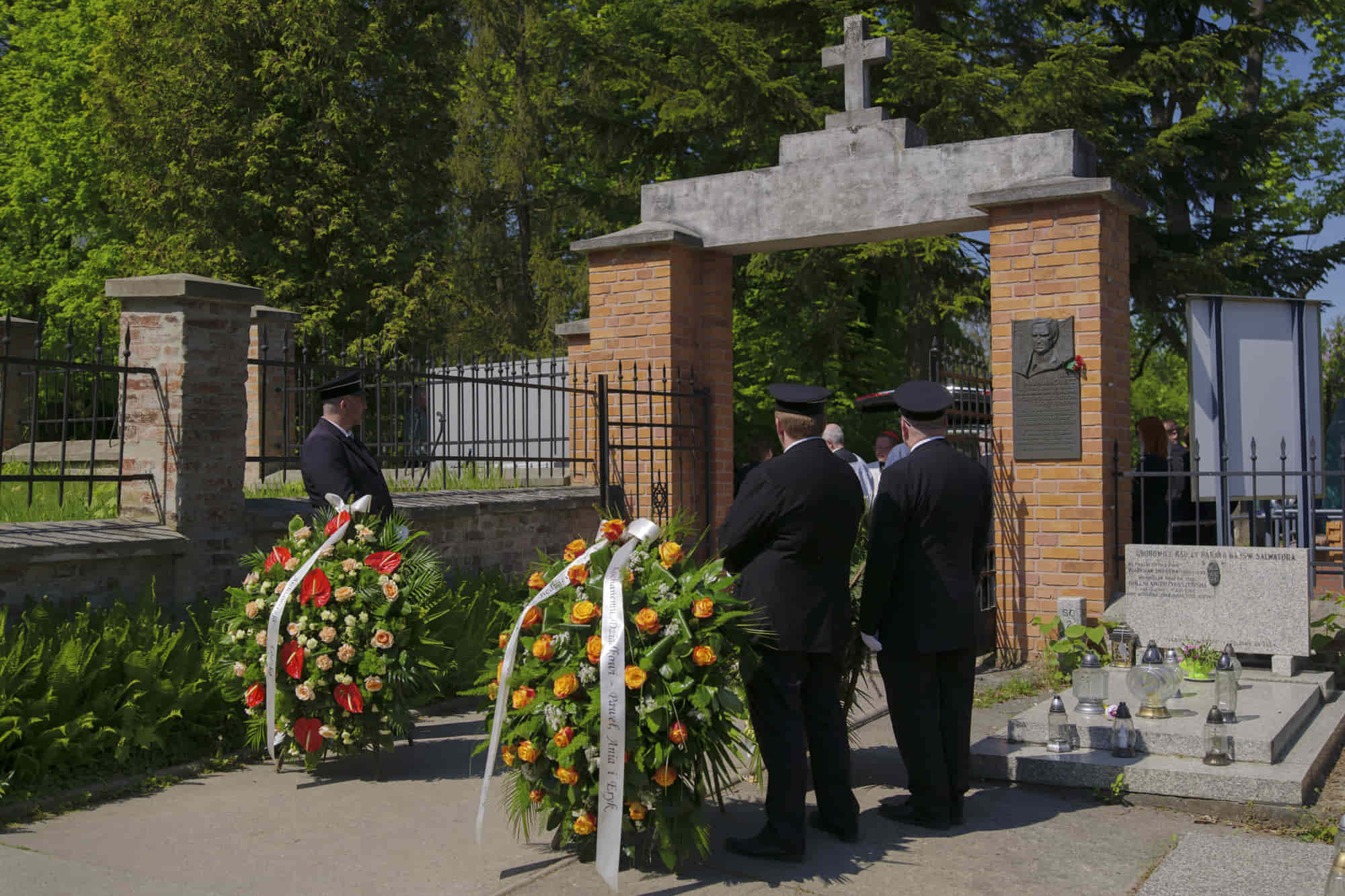 Wreaths at a cemetery gate on a sunny day, with Lilia staff nearby